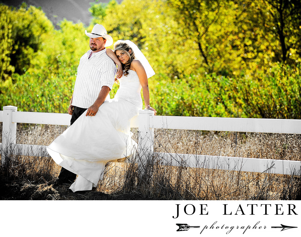 Country bride with groom wearing cowboy at together sitting on a fence.