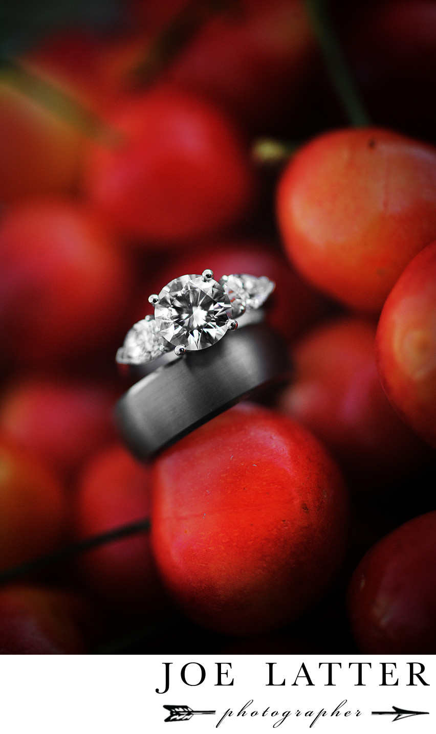 This is an image of a bride’s wedding ring and a groom’s wedding band photographed in a bowl of red cherries.
