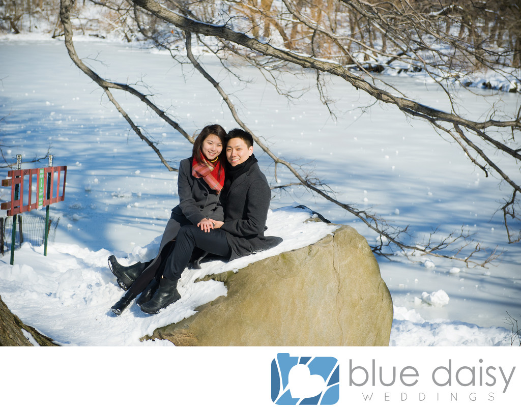 Engaged couple sitting on snow covered rock by the Lake