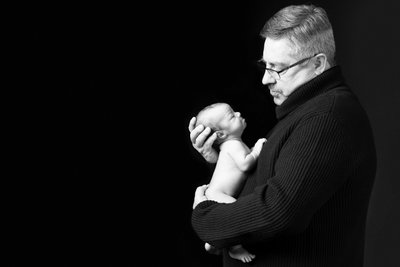 Grandfather’s Gentle Gaze: Holding Newborn Close