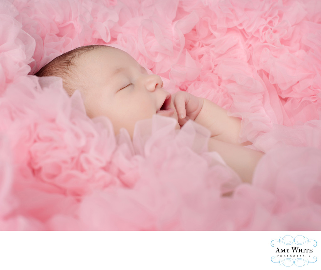 Happy newborn surrounded by pink ruffles 