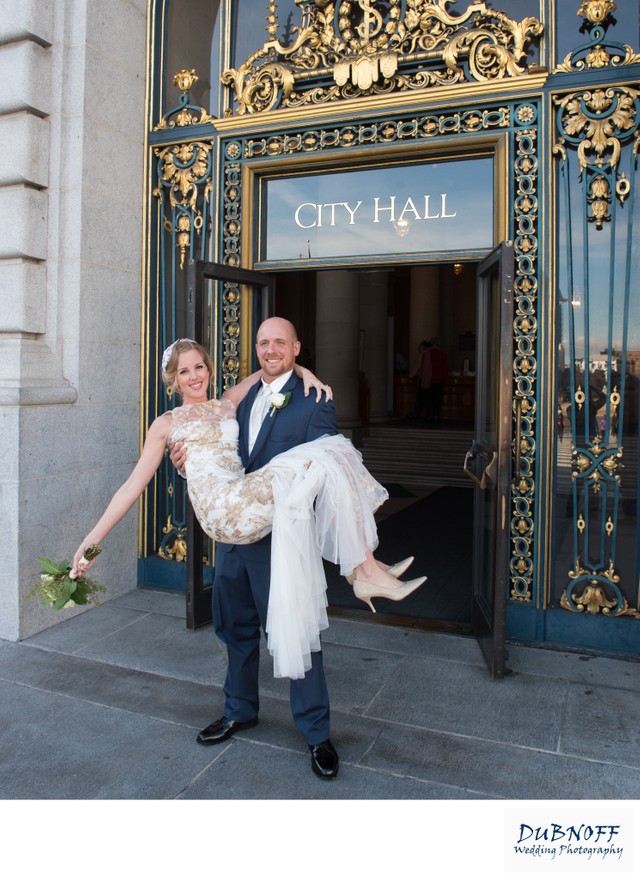 Groom lifting bride in front of SF City Hall Exit and  Entrance sign