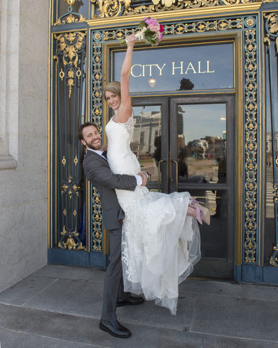 Bride Cheering in front of City Hall Sign with Bouquet in the air