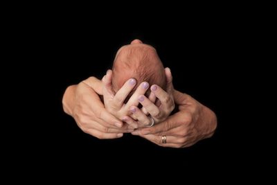 Baby's head in parents hands on black
