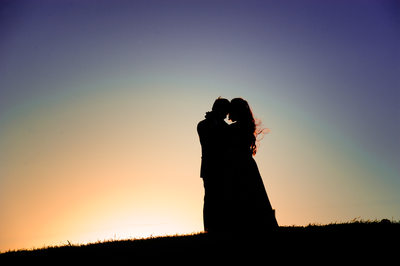 Silhouetted Couple Embracing on Hill with Sunset