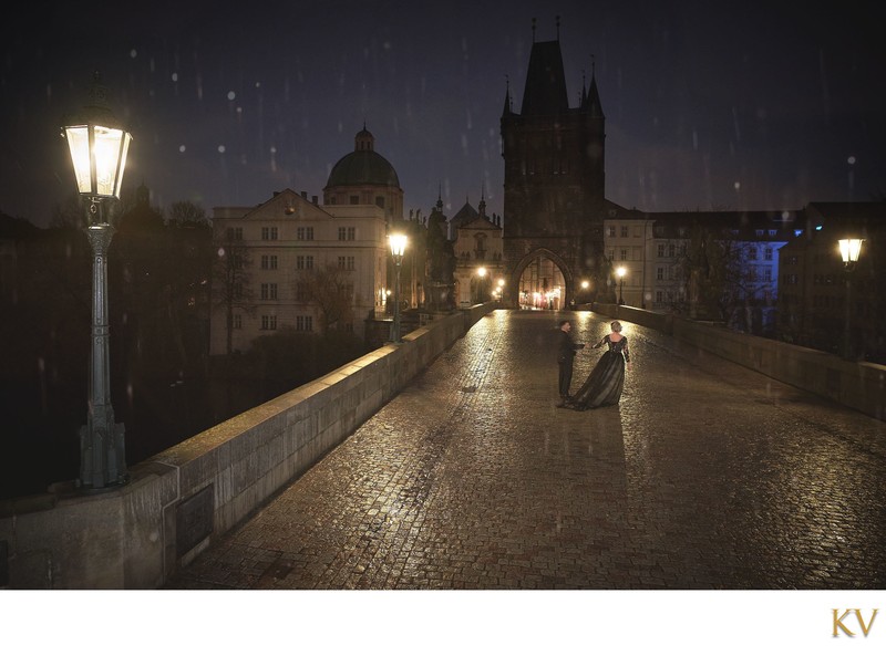 Gothic-dressed couple dancing atop Charles Bridge in the rain at night