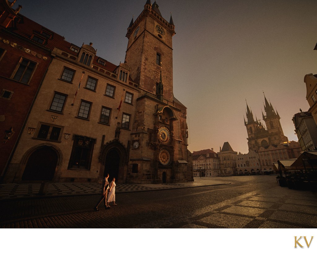 couple walk through Prague's historic Old Town Square at sunrise