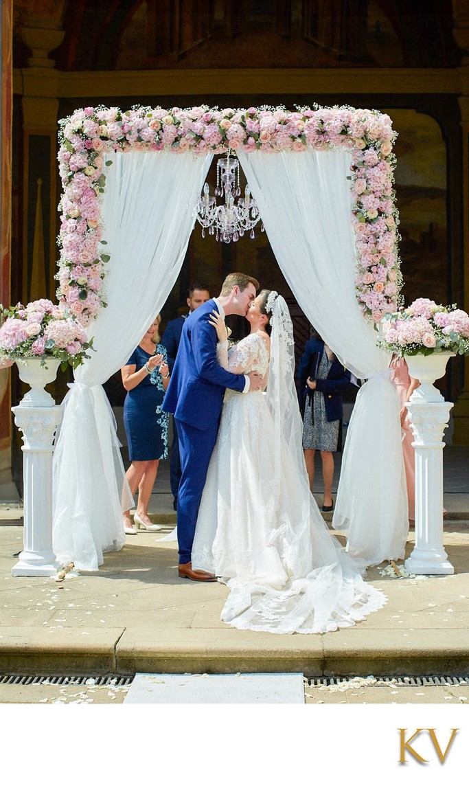 Newlyweds kiss under a chandelier at the Ledebour Garden in Prague