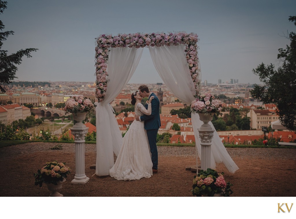 Newlyweds Embrace Above Prague Under Floral Arch