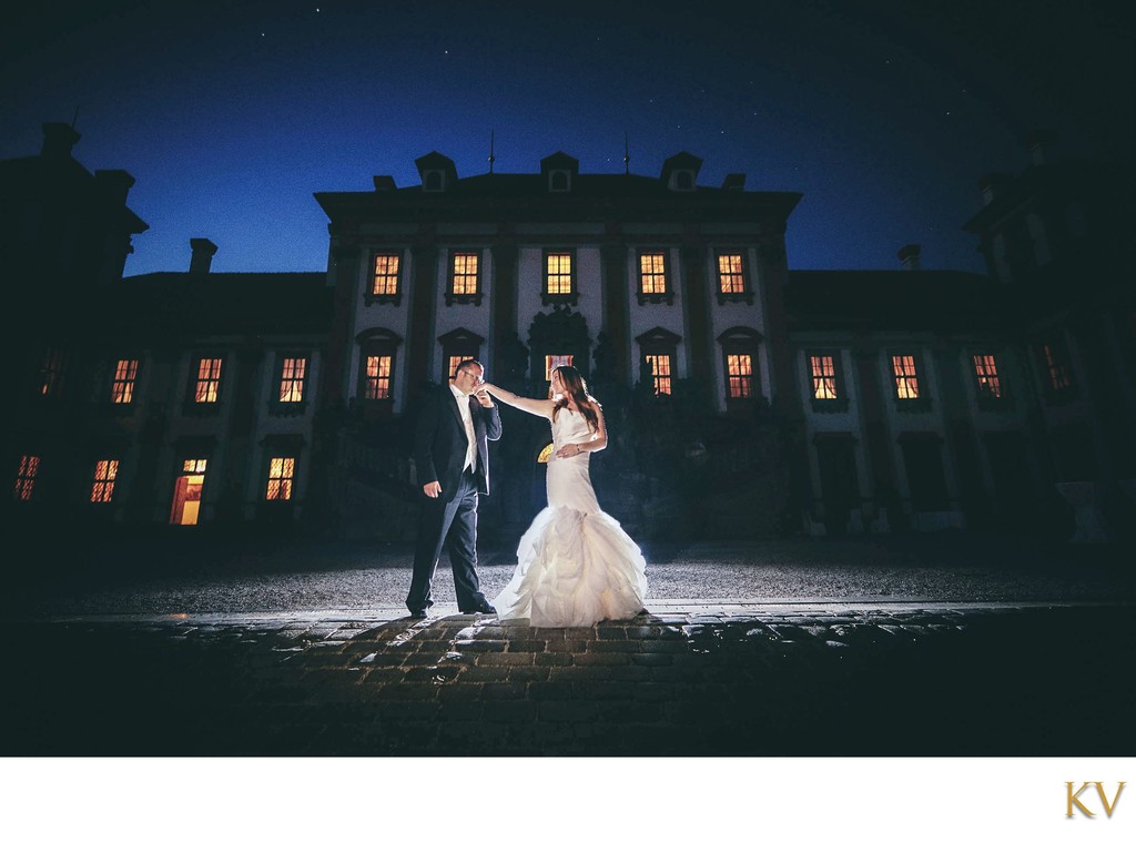 Groom kisses brides hand at night in front of Troja Palace