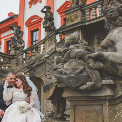 Under the statues at Troja Chateau wedding couple