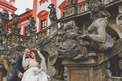 Under the statues at Troja Chateau wedding couple