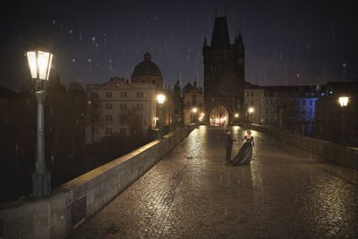 Gothic-dressed couple dancing atop Charles Bridge in the rain at night