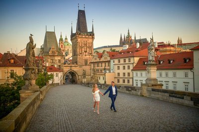 walking hand-in-hand across Charles Bridge at sunrise