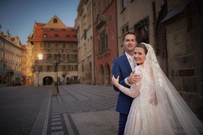 Newlyweds smile towards the camera at the Old Town Square at sunrise