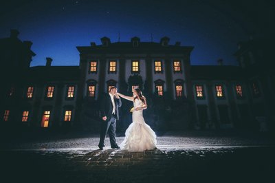 Groom kisses brides hand at night in front of Troja Palace