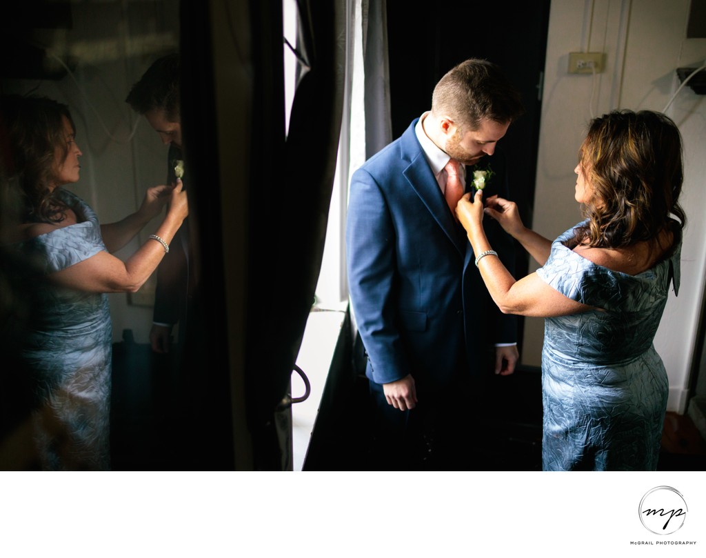 mother pinning boutonniere on groom with reflection