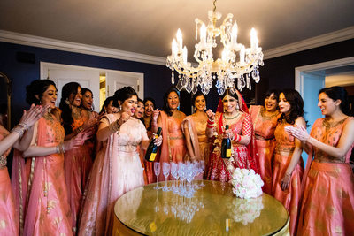 south asian bride popping champaign with bridesmaids in pink gowns